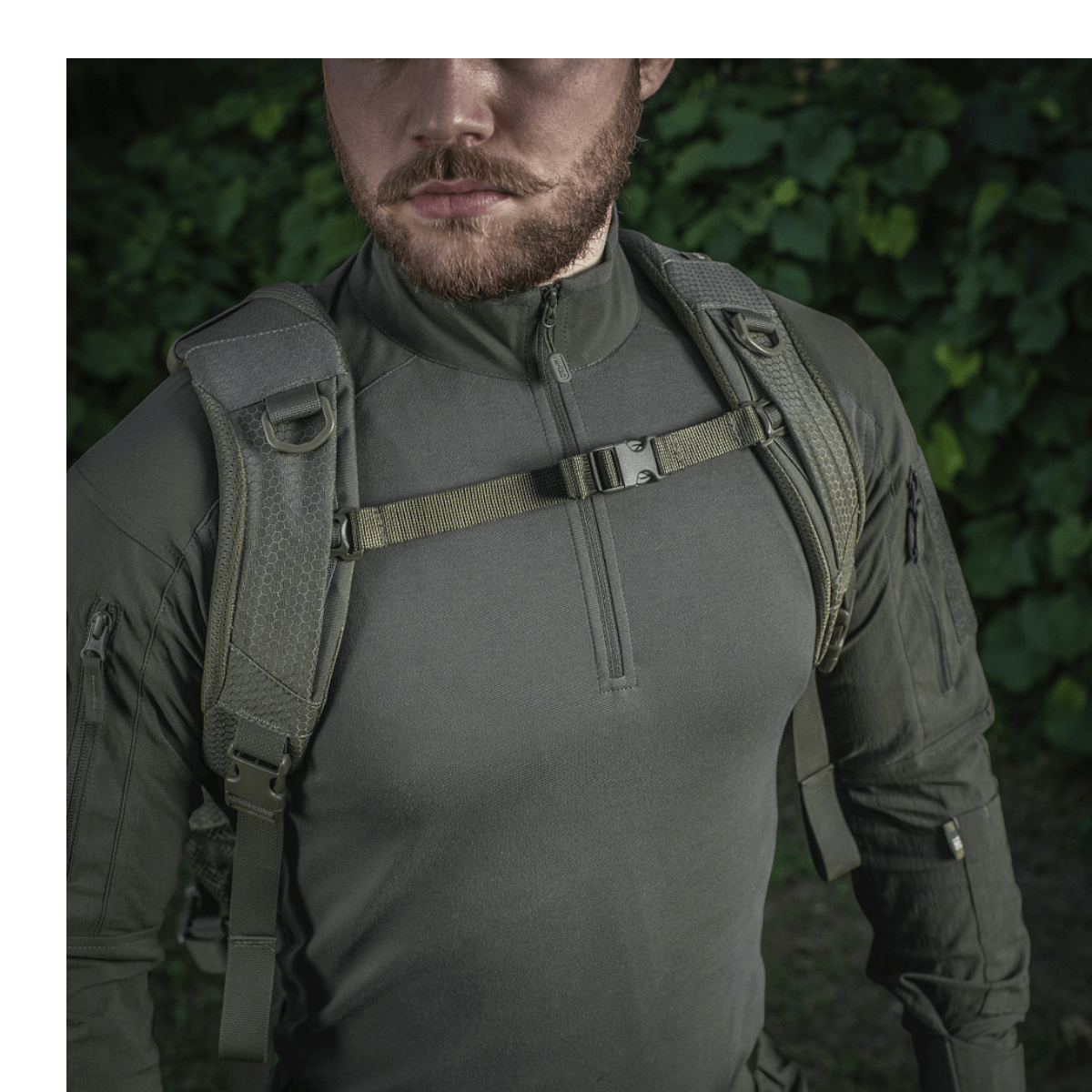 Mies pukeutuneena M-Tac Mission Rygsæk Elite Hex -reppuun, Cordura 1000D, ergonominen muotoilu ja MOLLE LASER CUT -järjestelmä metsäympäristössä.