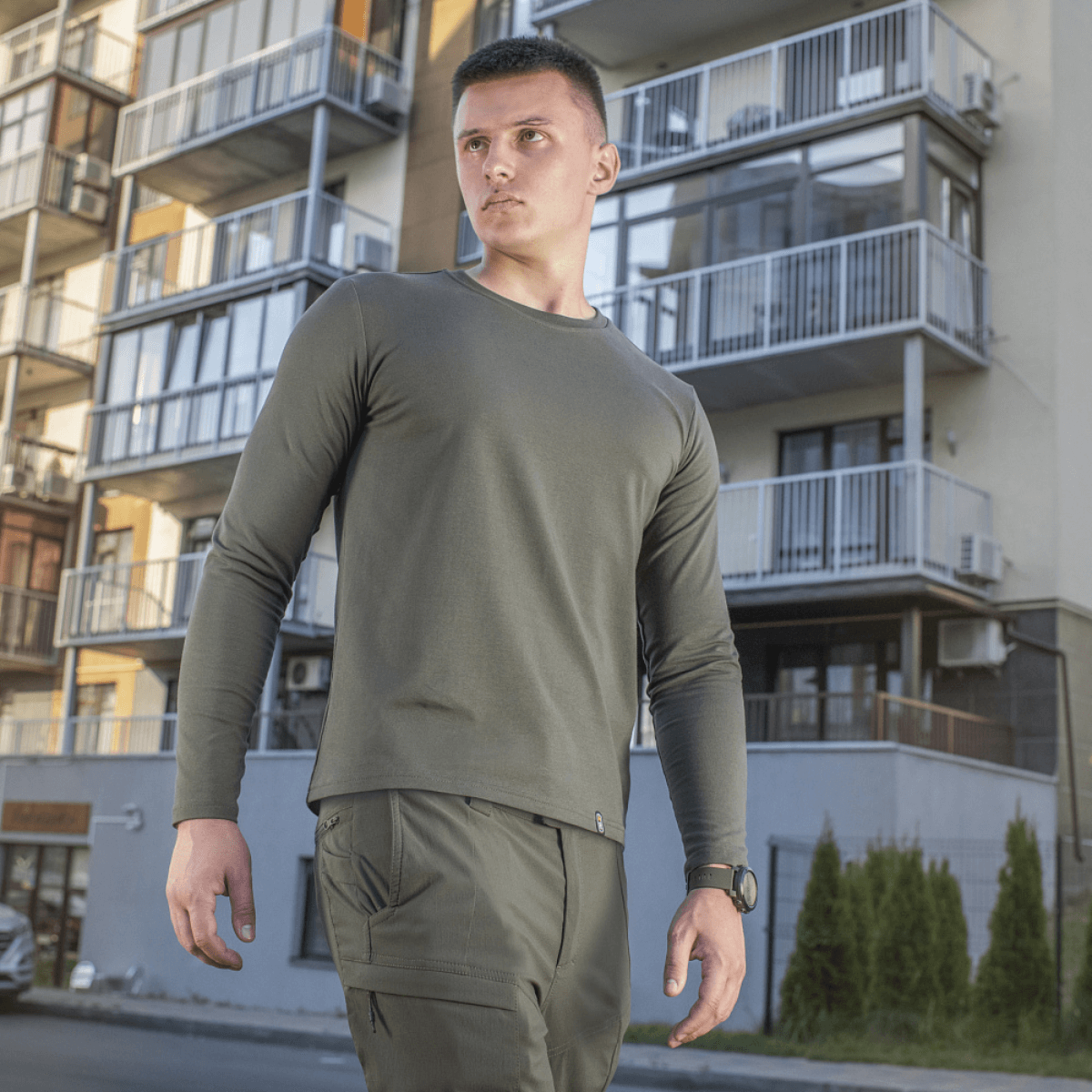 Mies M-Tac Long-sleeve T-shirt 93/7 päällä modernien rakennusten edessä, täydellinen arkeen, univormuihin ja ulkoiluun.
