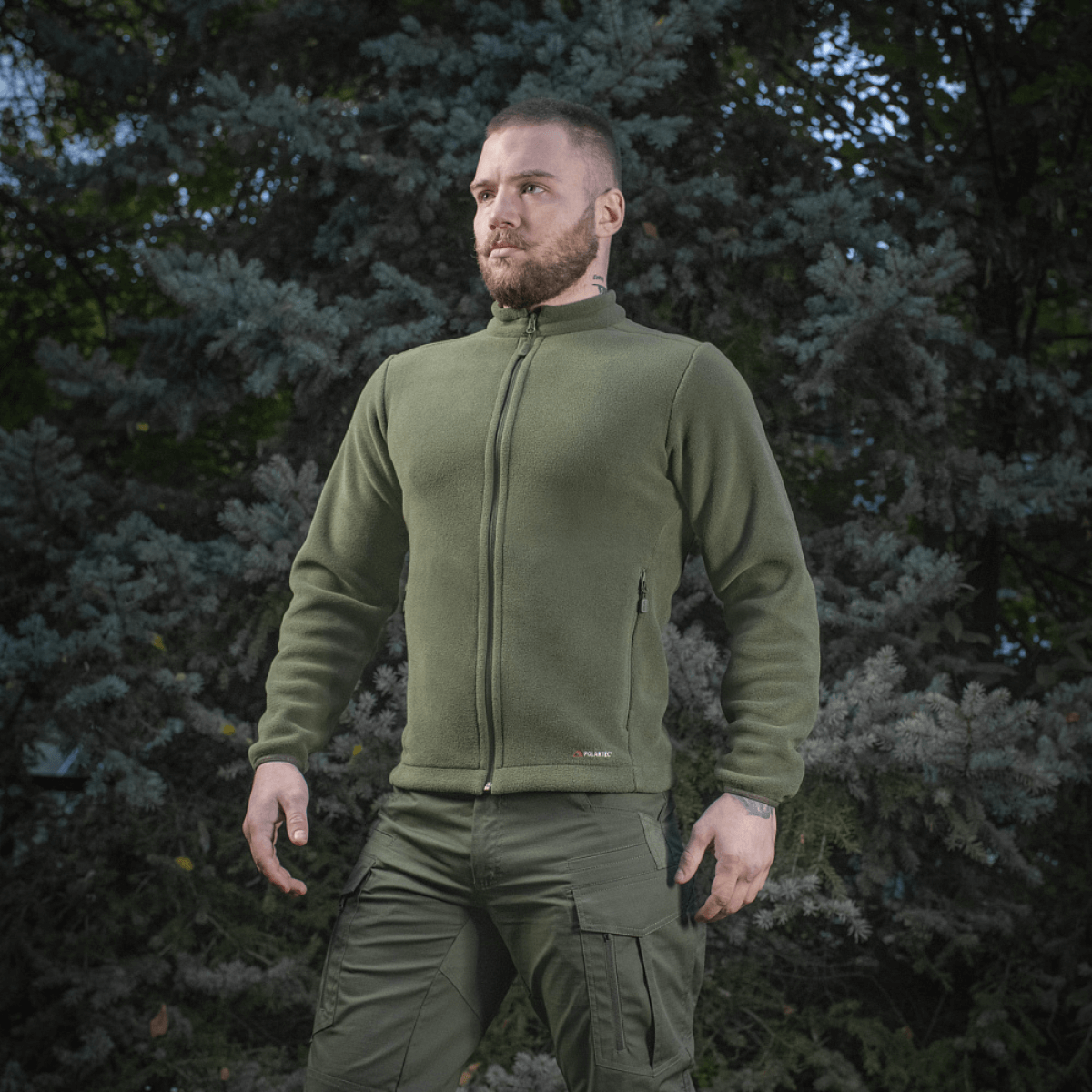 Mies pukeutuneena M-Tac Nord Polartec -fleecetakkiin metsätaustan edessä, näyttää takin käytön ulkona.