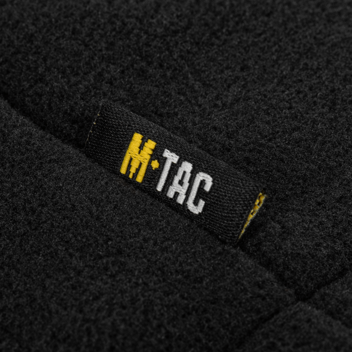 Etiketti M-Tac Combat Fleece Polartec -takissa mustasta fleecemateriaalista M-Tac-logolla. Sopii taktiseen ja arkikäyttöön. Korkea laatu.