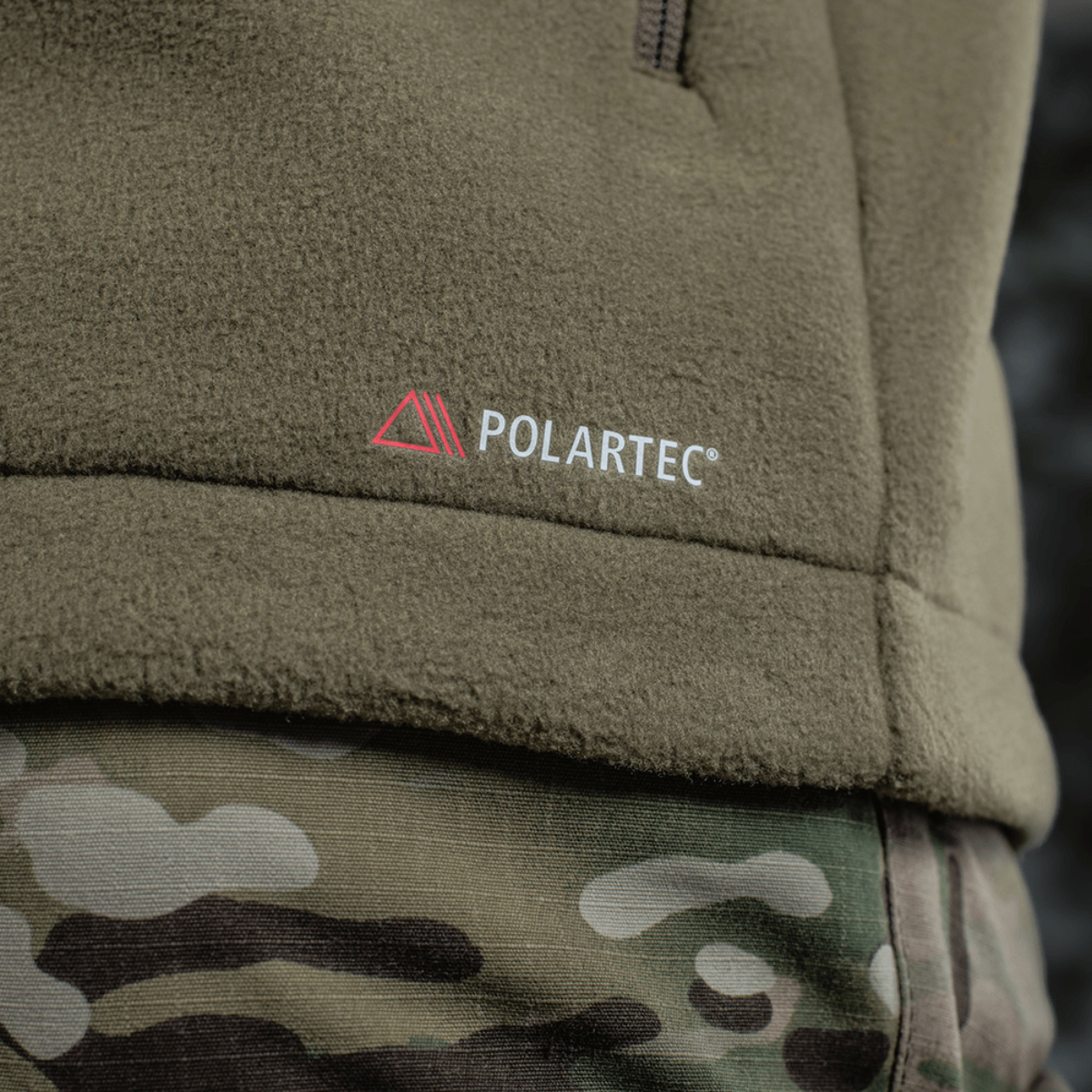 Yksityiskohta M-Tac Combat Fleece Polartec -takista Polartec-logolla, maastokuvio ja fleece-materiaali, sopii taktiseen ja arkipukeutumiseen.