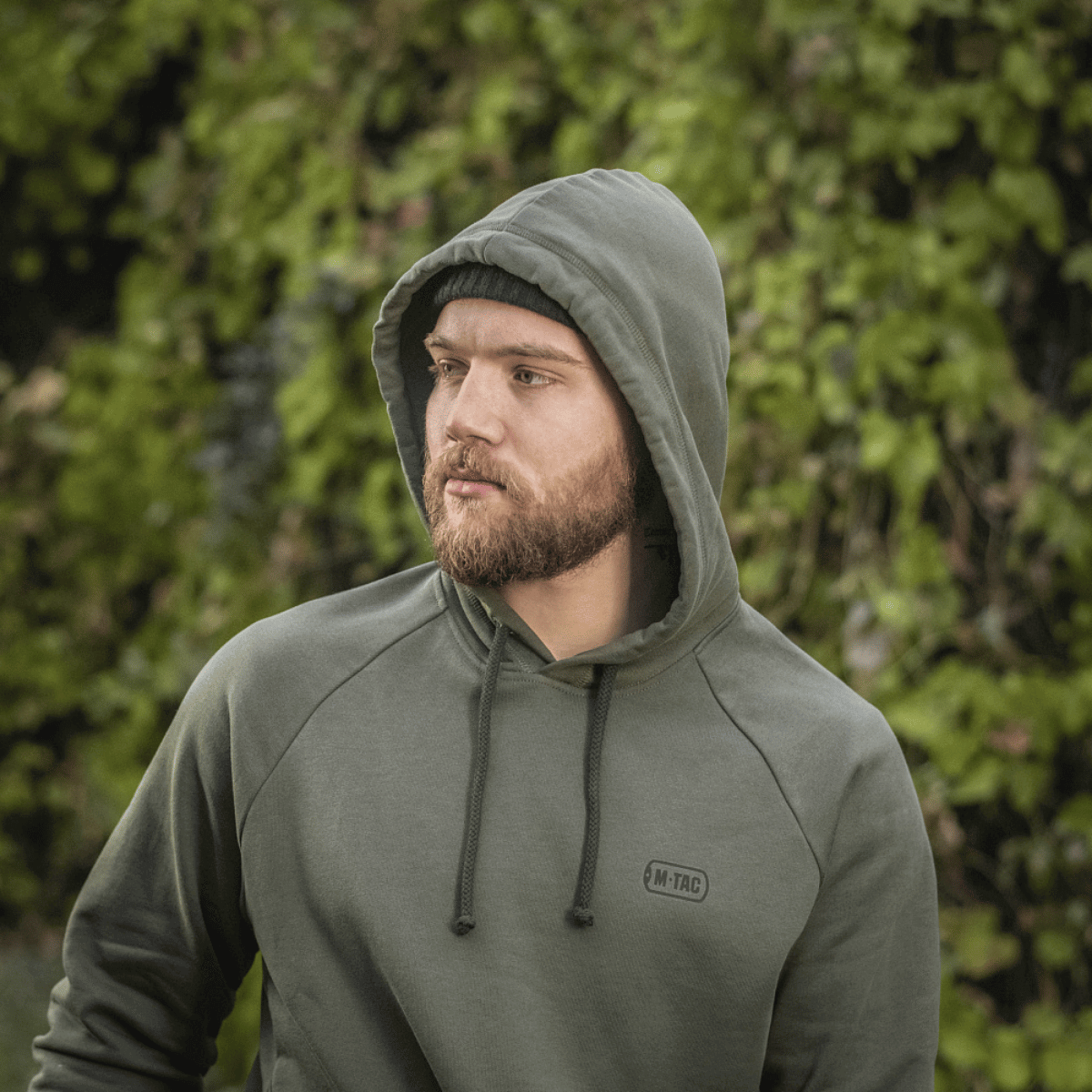 Mies M-Tac Cotton Raglan -hupparissa ulkoilmassa vihreässä ympäristössä.