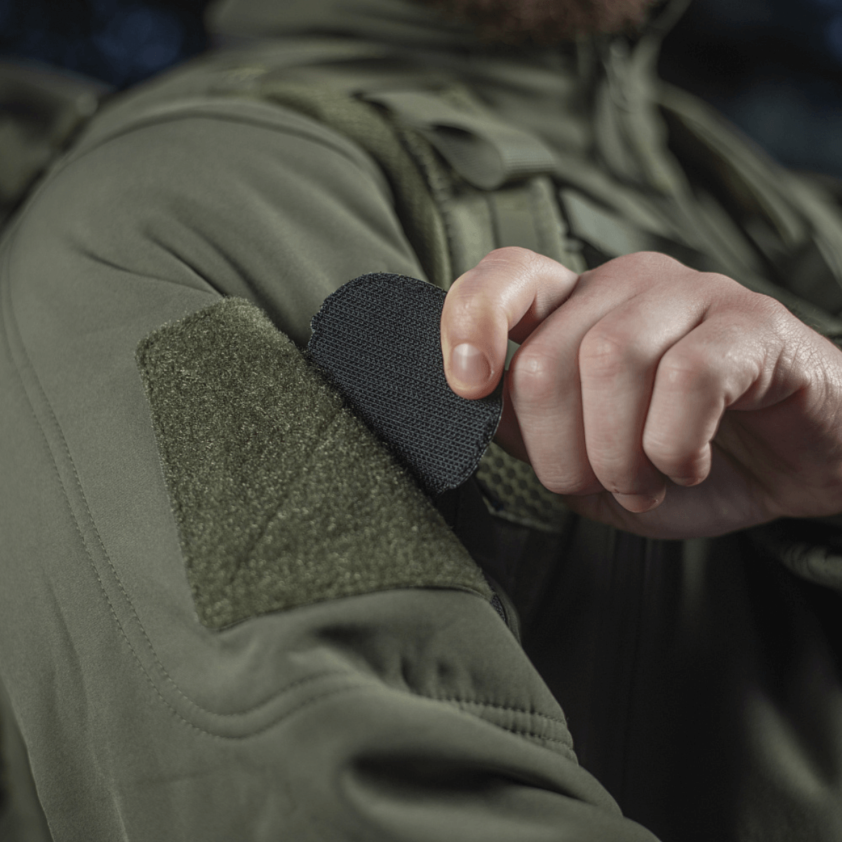 Henkilö kiinnittää M-Tac Patch Operator 3D PVC:n Velcro-kiinnityksellä takkiin, taktinen muotoilu, moraalimerkki, 6x7 cm, PVC.