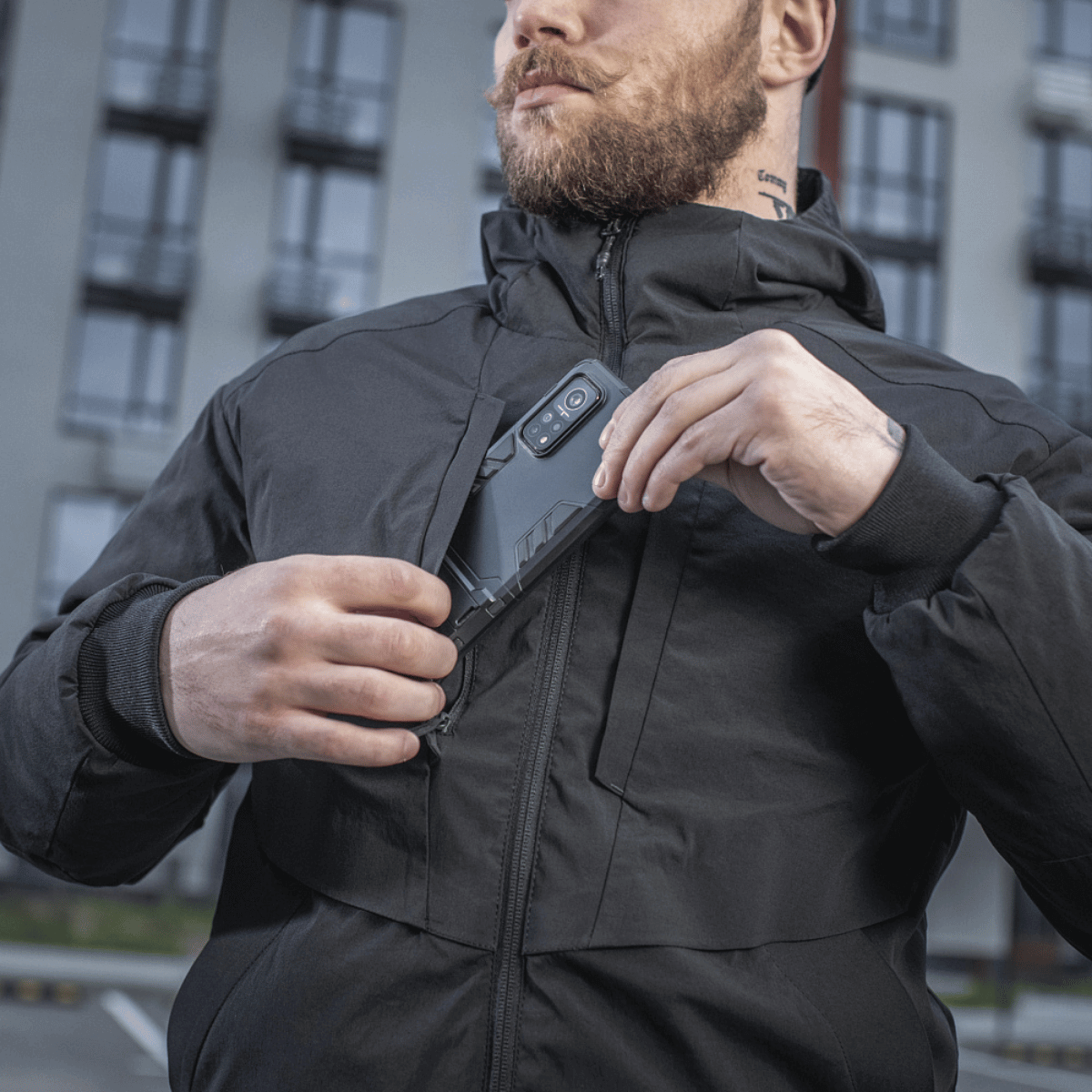 Mies pukeutuneena M-Tac Rubicon Jakke Gen. II -takkiin, näyttää takin kestävän Cordura-kankaan ja käytännöllisen rintataskun kaupunkiympäristössä.