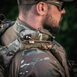 M-Tac Tourniquet Pouch Elastisk med MOLLE Gen.II taktiikkapukuisen miehen olkapäällä ulkona, nopea pääsy.