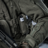 M-Tac Elastinen turnikekotelo Molle Gen.III kiinnitetty taktiseen liiviin metsäisessä ympäristössä, C-A-T tourniquet näkyvissä.