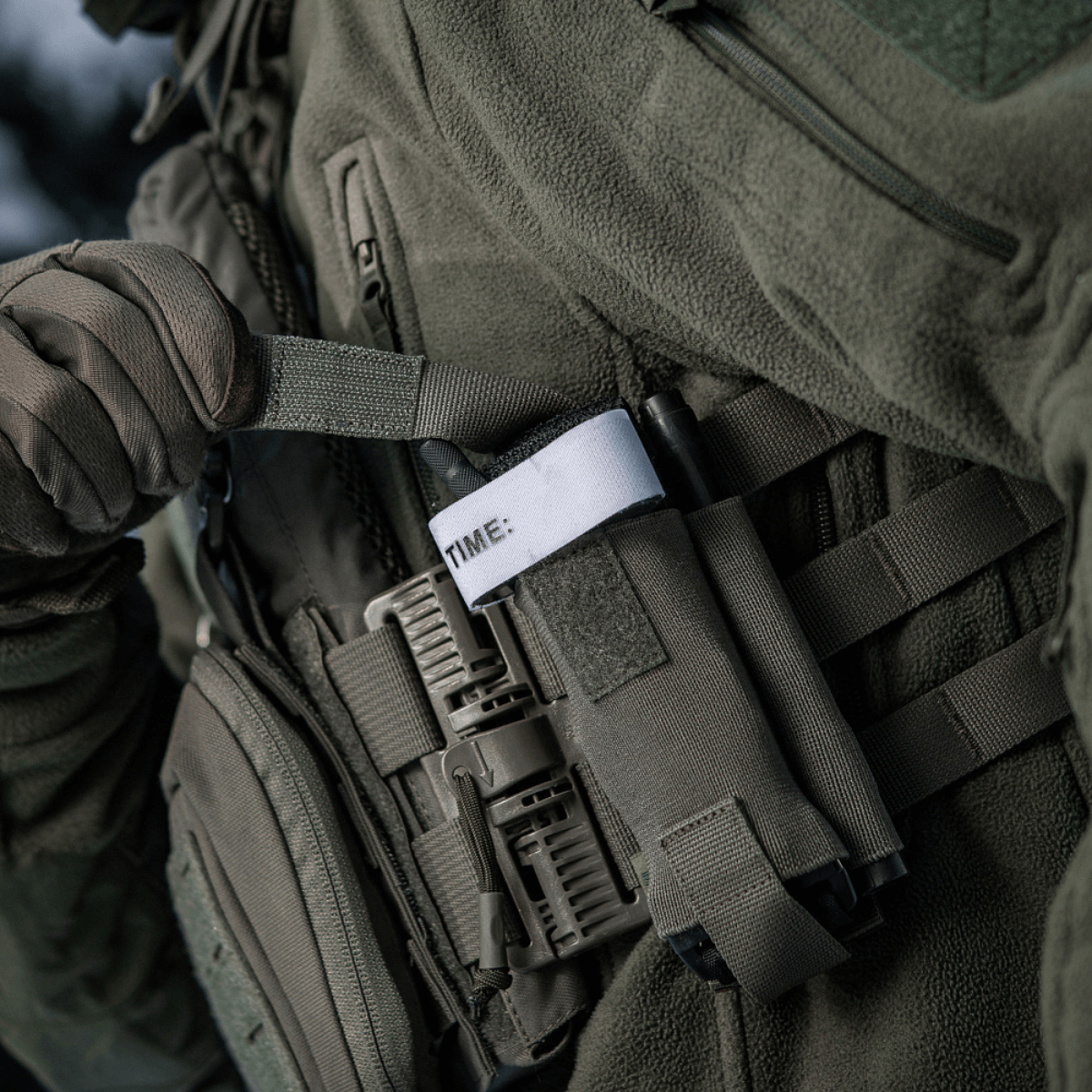 M-Tac Elastinen turnikekotelo Molle Gen.III kiinnitetty taktiseen liiviin, näyttää käytännöllistä käyttöä ja helpon pääsyn tourniquettiin.