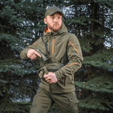 Mies kantaa M-Tac Sphaera Hex Hardsling Gen.II Elite -laukkua metsässä, valmis nopeaan toimintaan piilotetulla kantojärjestelmällä.