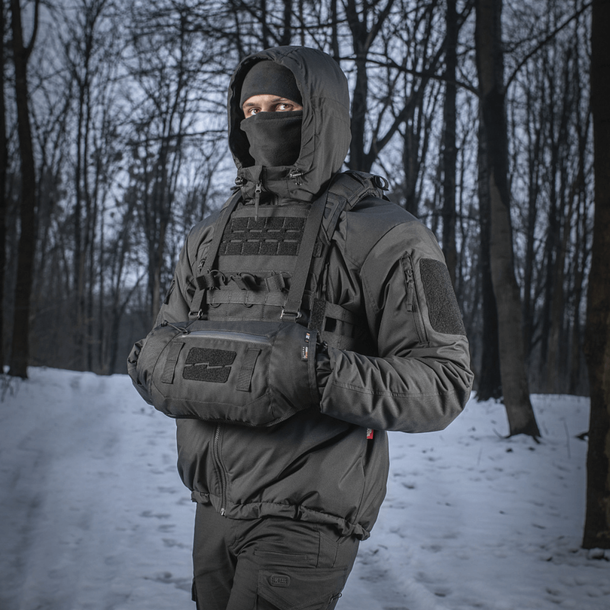 Henkilö käyttää M-Tac taktista käsilämmitintä Elite lumisessa metsässä, pitää kädet lämpiminä kylmässä säässä.