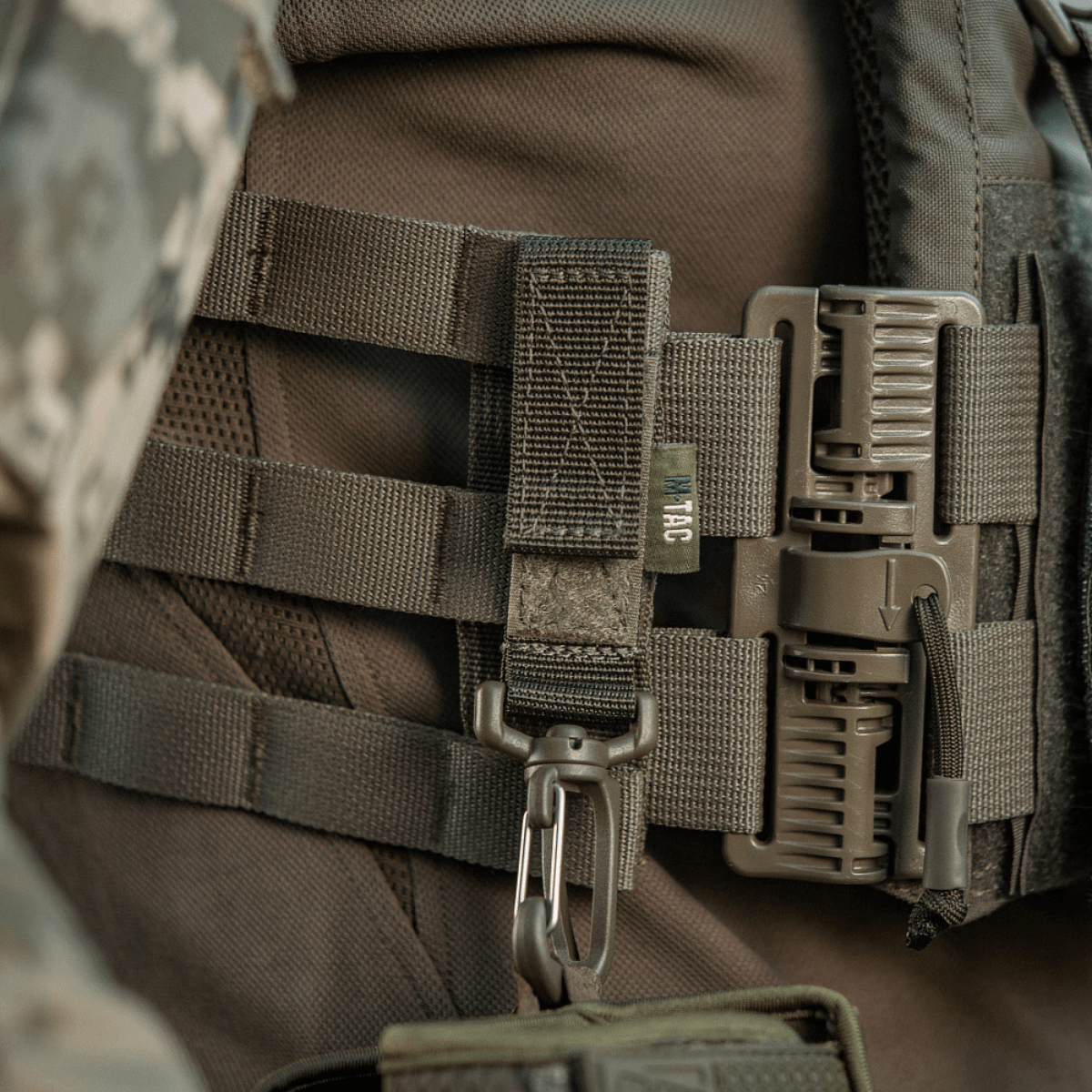 M-Tac karabiinihaka-lisävaruste kiinnitetty taktiseen MOLLE-reppuun lisävarusteille. Säädettävä Velcro-remmi kiinnitystä varten.