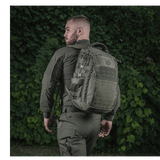 Henkilö M-Tac Mission Rygsæk Elite Hex -repun kanssa, taustalla vihreää kasvillisuutta.