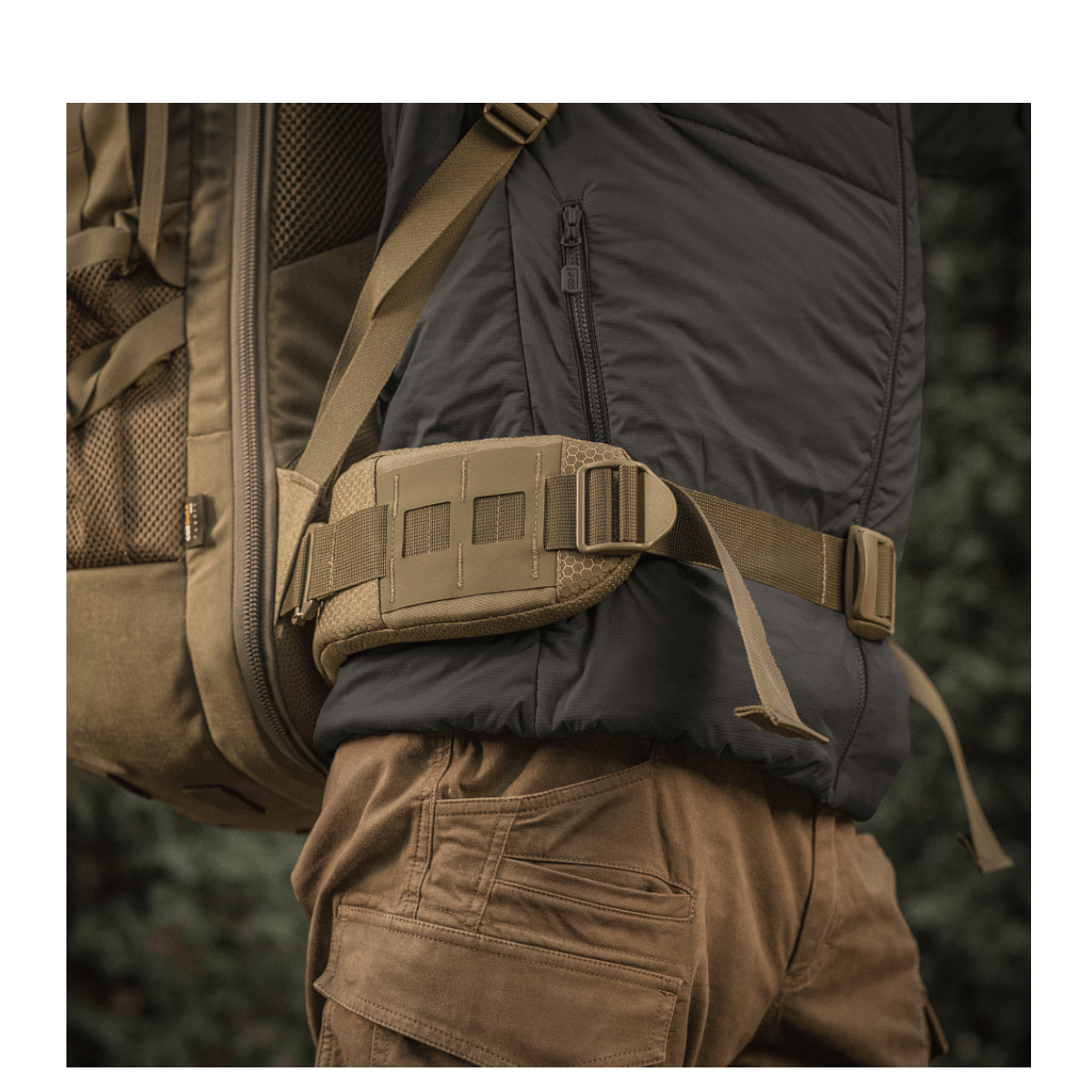 M-Tac reppu Large Elite Hex Gen. IV kantaa henkilö selässä ulkovaatteissa, sivulta luonnollisessa ympäristössä.