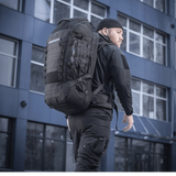 Mies kantaa M-Tac Rygsæk Large Elite Hex Gen. IV -reppua mustana, ergonomisesti suunniteltu toiminnallisuuteen ja kestävyyteen, nähty kaupunkiympäristössä.