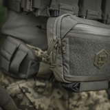 M-Tac Large Elite Gen.II olkalaukku Cordura 500D:stä YKK-vetoketjuilla, sopii taktiseen käyttöön, nähty maastotaustalla.