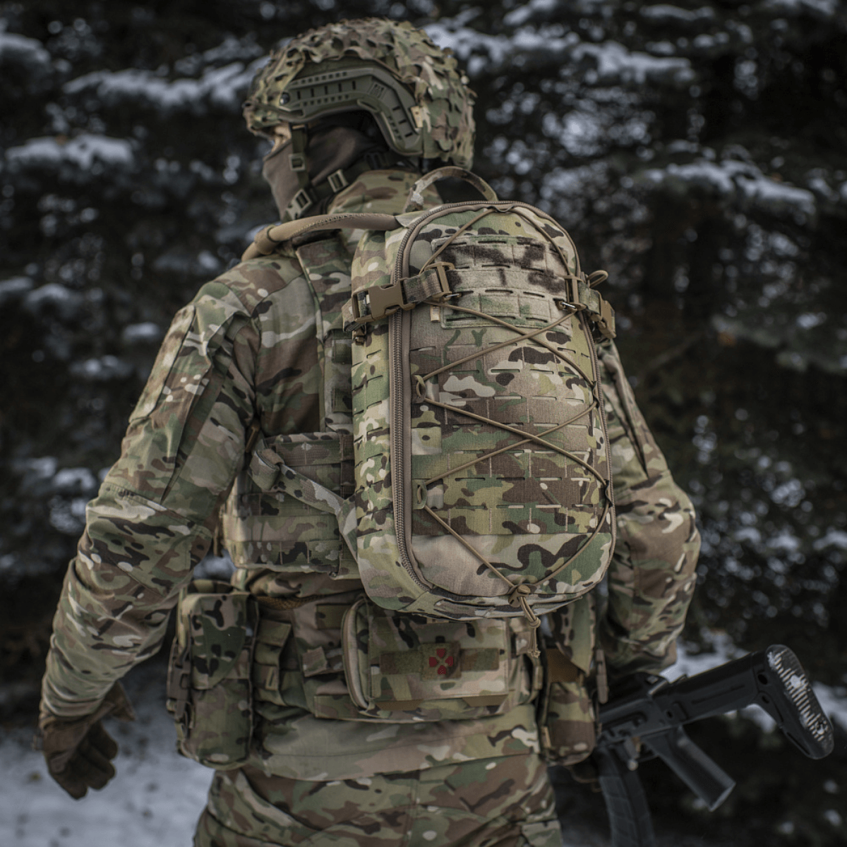 Sotilas kantaa M-Tac reppu Sturm Elite Gen.II lumisessa metsässä, MOLLE Laser Cut -järjestelmä ja joustonaru varusteille.
