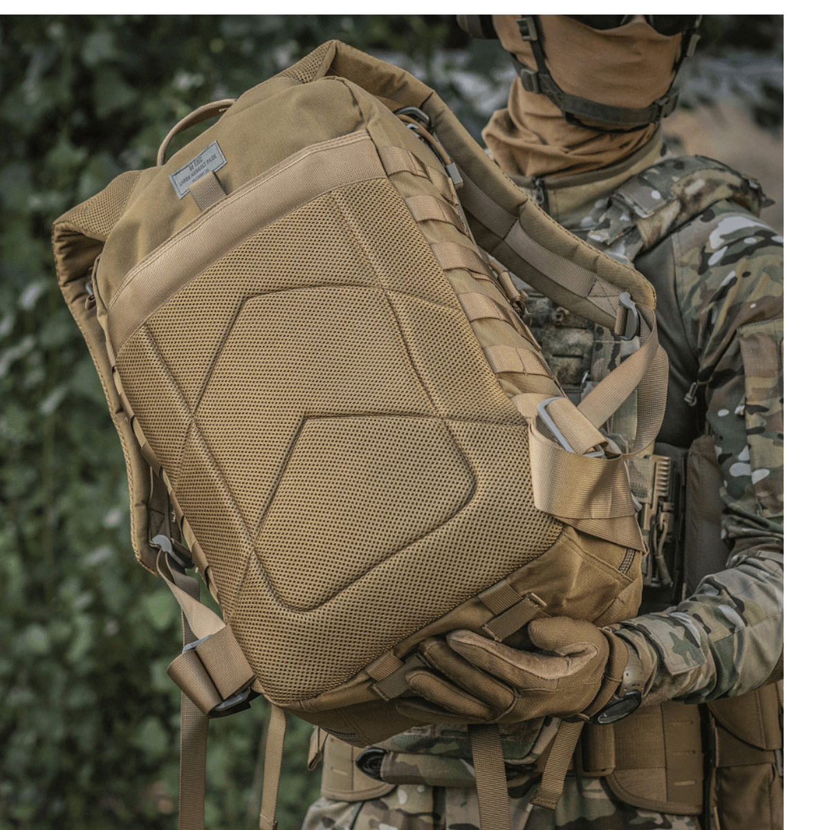 Sotilas M-Tac Large Assault Pack -repun kanssa urbaanissa maastokuviossa, näyttää MOLLE-kiinnityksen ja mukavat olkahihnat.