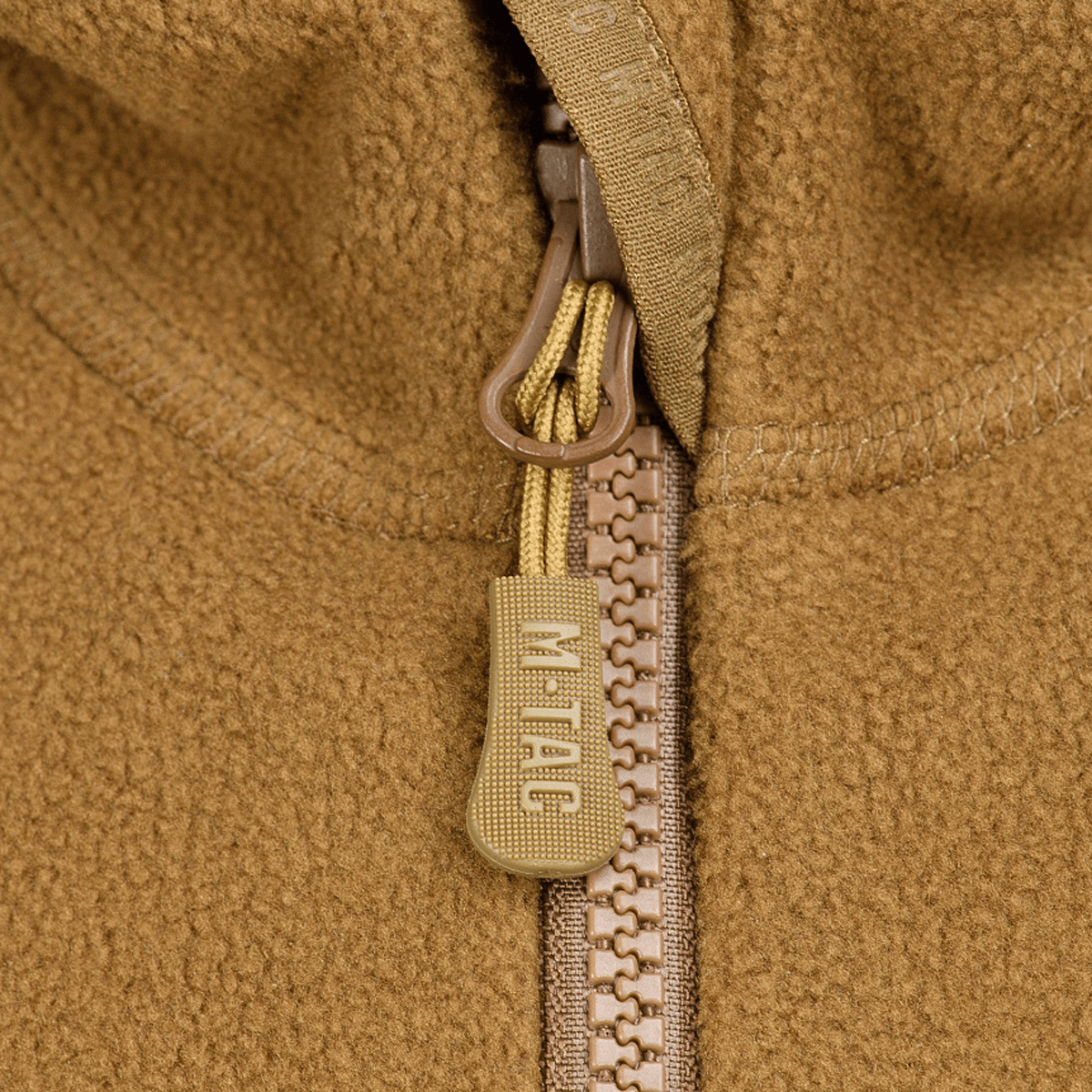 Lähikuva vetoketjusta M-Tac Lite Microfleece Hættetrøje -tuotteessa M-Tac-logolla, näyttää yksityiskohtia hengittävästä ja joustavasta materiaalista.