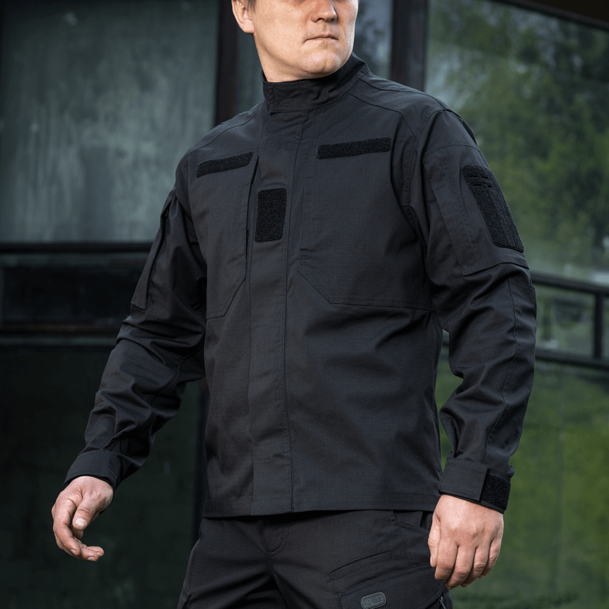 Mies pukeutuneena mustaan M-Tac Patrol Flex -takkiin velcro-paneeleilla, piilotetuilla rintataskuilla ja tuuletusrei'illä taktista käyttöä varten
