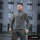 Mies M-Tac Nord Polartec -fleecetakissa, suunniteltu tyyliin ja lämpöön, Polartec® 200 Series -fleecellä asuinrakennuksen taustalla.