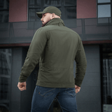 Mies M-Tac Flash -takissa modernin rakennuksen edessä. Kevyt ja monikäyttöinen takki arkeen ja aktiviteetteihin. Ei tarrapaloja hihoissa.