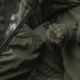 Henkilö M-Tac Stalker Gen.III -takissa, puhelin taskussa, säätää takkia, näyttää tyyliä ja toiminnallisuutta.