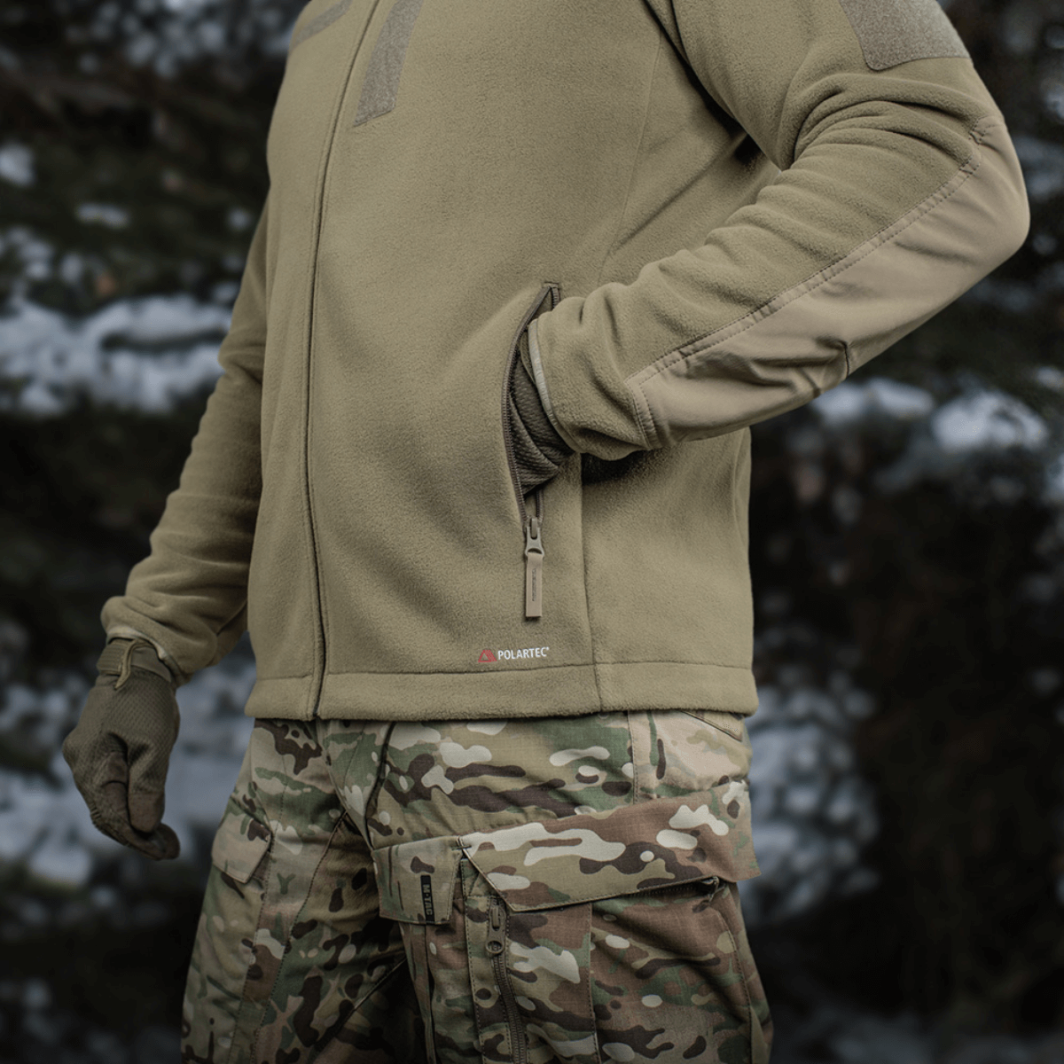 Henkilö metsässä pukeutuneena M-Tac Combat Fleece Polartec -takkiin, maastohousut ja hanskat mukana.