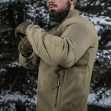 Mies metsässä pukeutuneena M-Tac Combat Fleece Polartec -takkiin, korostaa taktista muotoilua.