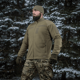 Mies pukeutuneena M-Tac Combat Fleece Polartec -takkiin metsässä, korostaa taktikointiin sopivaa muotoilua.