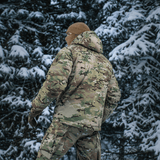 M-Tac Alpha Gen.IV Pro Primaloft -talvitakki lumipeitteisessä metsässä Multicam-designilla, tarjoaa äärimmäistä kestävyyttä ja kylmäsuojaa.