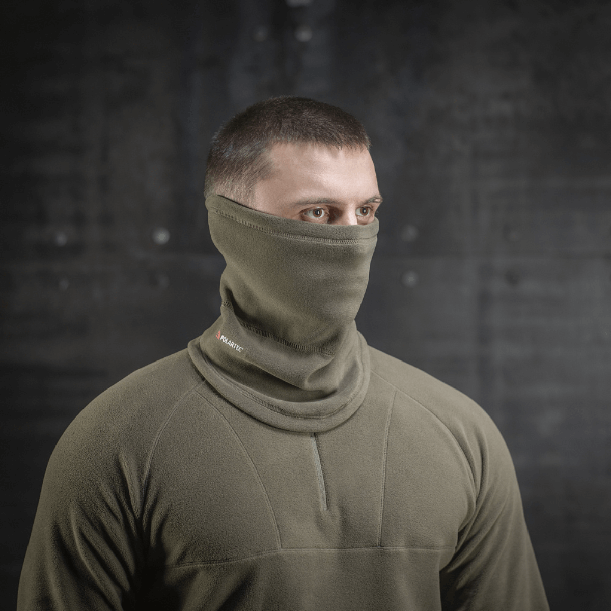 Miehellä on M-Tac Polartec Anatomic Tube Scarf oliivinvihreänä, monikäyttöinen huivi joka suojaa tuulelta ja kylmältä.