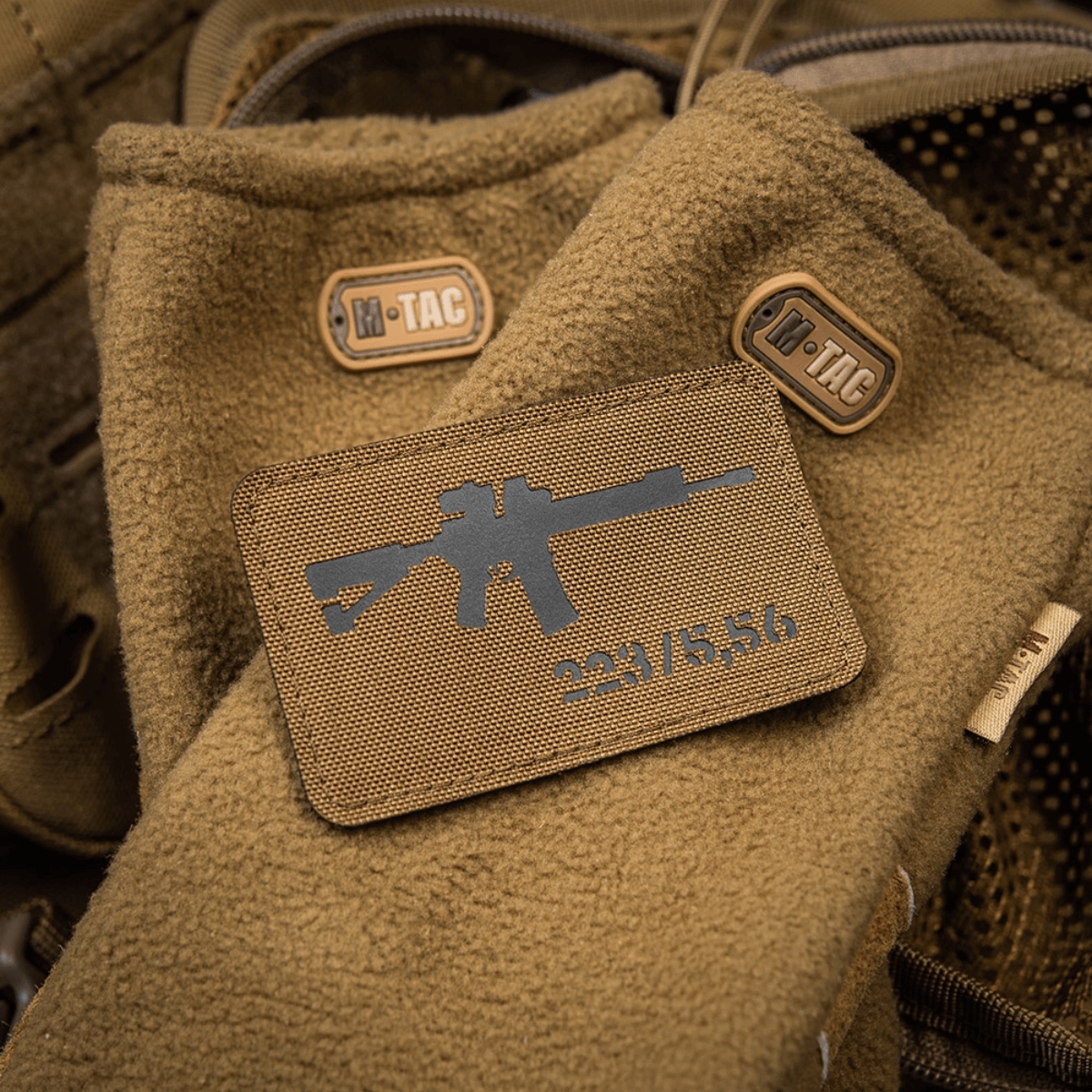 M-Tac AR-15 223/5,56 Laser Cut Patch, kiinnitetty ruskeaan taktiseen peitteeseen M-Tac-logolla, suunniteltu ulko- ja sotilaskäyttöön.