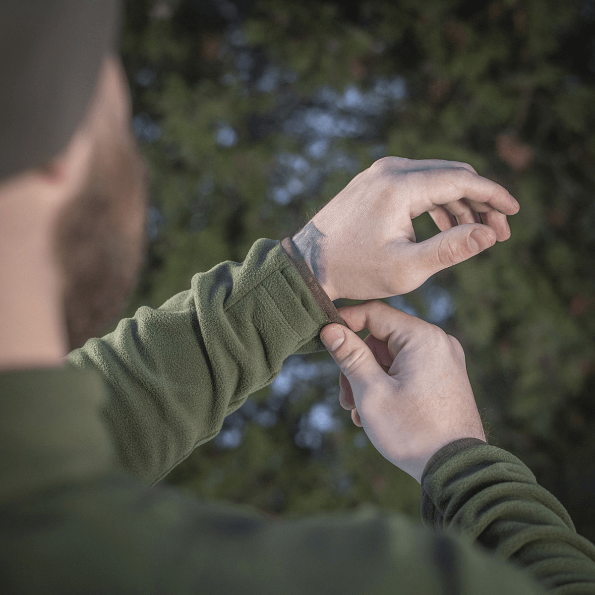Mies säätää hihansuutta M-Tac Delta Polartec fleece-takissa metsässä, näyttää takin toiminnallisen suunnittelun ja materiaalin.