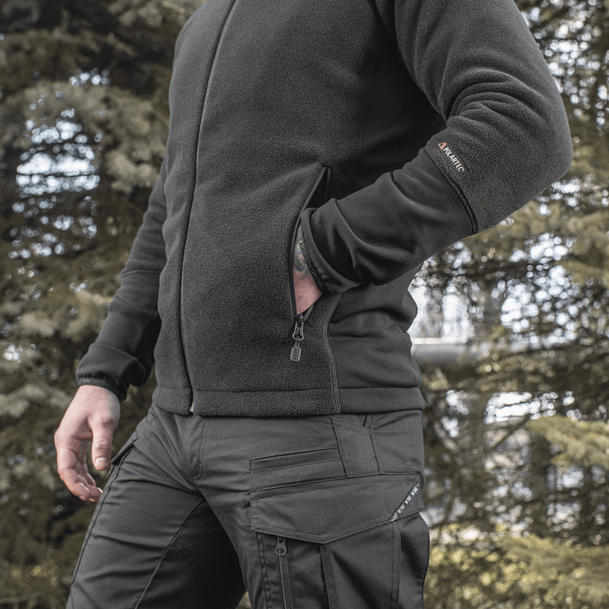 Mies pukeutuneena M-Tac Polartec Sport -fleecatakkiin metsässä, toimii lämpimänä ja toiminnallisena välikerroksena viileään säähän.