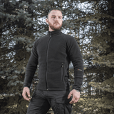 Mies pukeutuneena M-Tac Polartec Sport -fleecatakkiin mustana, sopii vaihtokauteen ja viileään säähän, ympäröity puita.