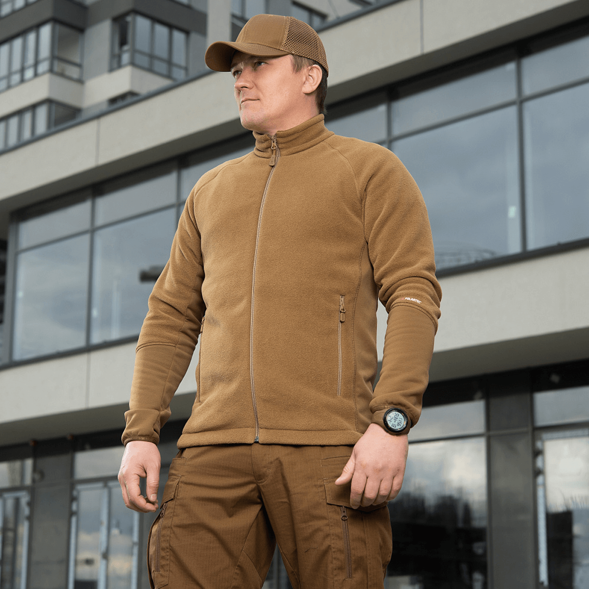 Mies, jolla on M-Tac Polartec Sport Fleecejakke, seisoo modernin rakennuksen edessä, sopiva siirtymäkaudelle ja kylmälle säälle