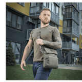 Mies kantaa M-Tac Konvert Taske Eliteä harmaassa kaupunkiympäristössä, moderni tablettilaukku valmistettu Cordura-materiaalista.