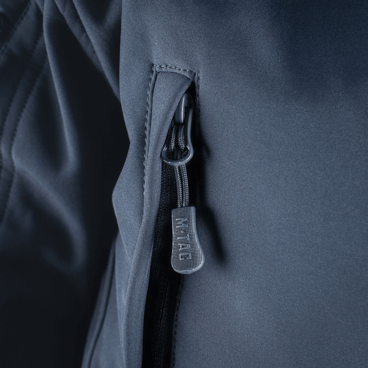 Lähikuva M-Tac Soft Shell -takin vetoketjusta, näyttää vesihylkivän kankaan yksityiskohdat ja vahvan vetoketjun mekanismin.