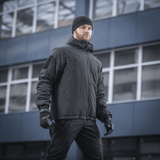 Mies pukeutuneena M-Tac Alpha Gen.III Pro -talvitakkiin kaupunkiympäristössä, sopii äärimmäisiin olosuhteisiin mukavuudella ja vettä hylkivällä materiaalilla.