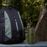 M-Tac 450 ml termosmuki venttiilillä pöydällä repun vieressä metsäkohtauksessa