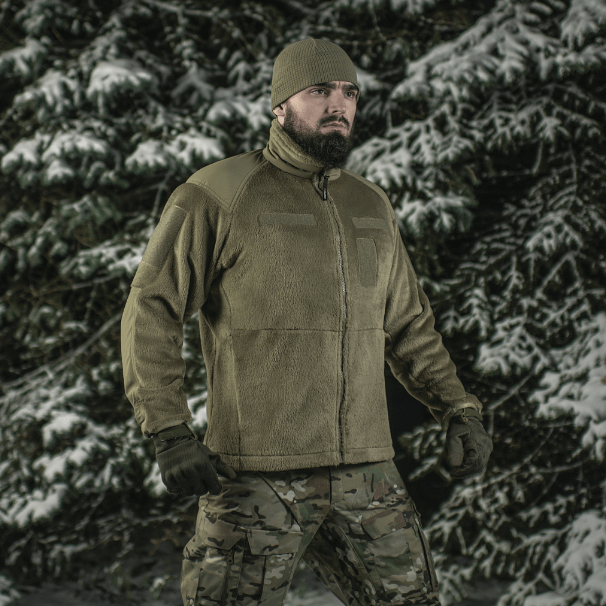 Mies metsässä kantaa M-Tac Battle Fleece Polartec -takkia, sopii sotilas- ja poliisikäyttöön, korostaa mukavuutta ja kestävyyttä talvisessa maisemassa.