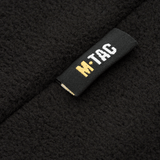 Lähikuva M-Tac Delta Fleece -takin etiketeistä, musta ja keltainen logo, fleece-materiaali, ihanteellinen ulkoiluun ja kylmiin olosuhteisiin