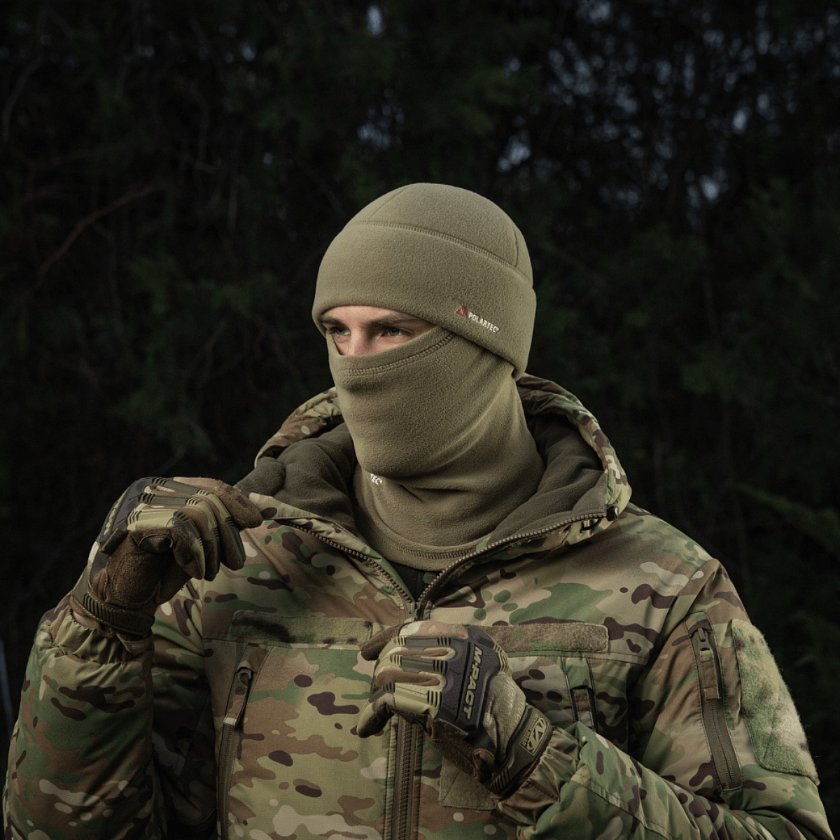 Henkilö pukeutuneena M-Tac Fleece Polartec Watch Cap -pipoon kylmässä ulkoilmassa, sopii talviaktiviteetteihin, maastokuvioinen takki.