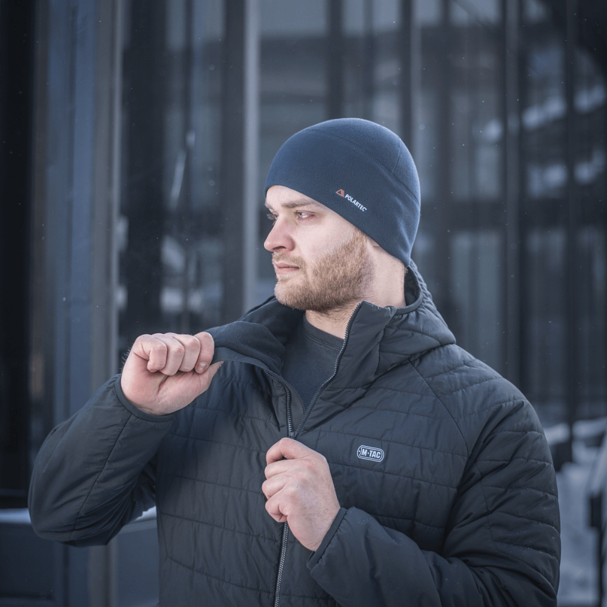 Mies pukeutunut M-Tac Fleece Watch Cap Light Polartec talvihattu, seisoo ulkona kylmässä säässä en lämmin takki yllä