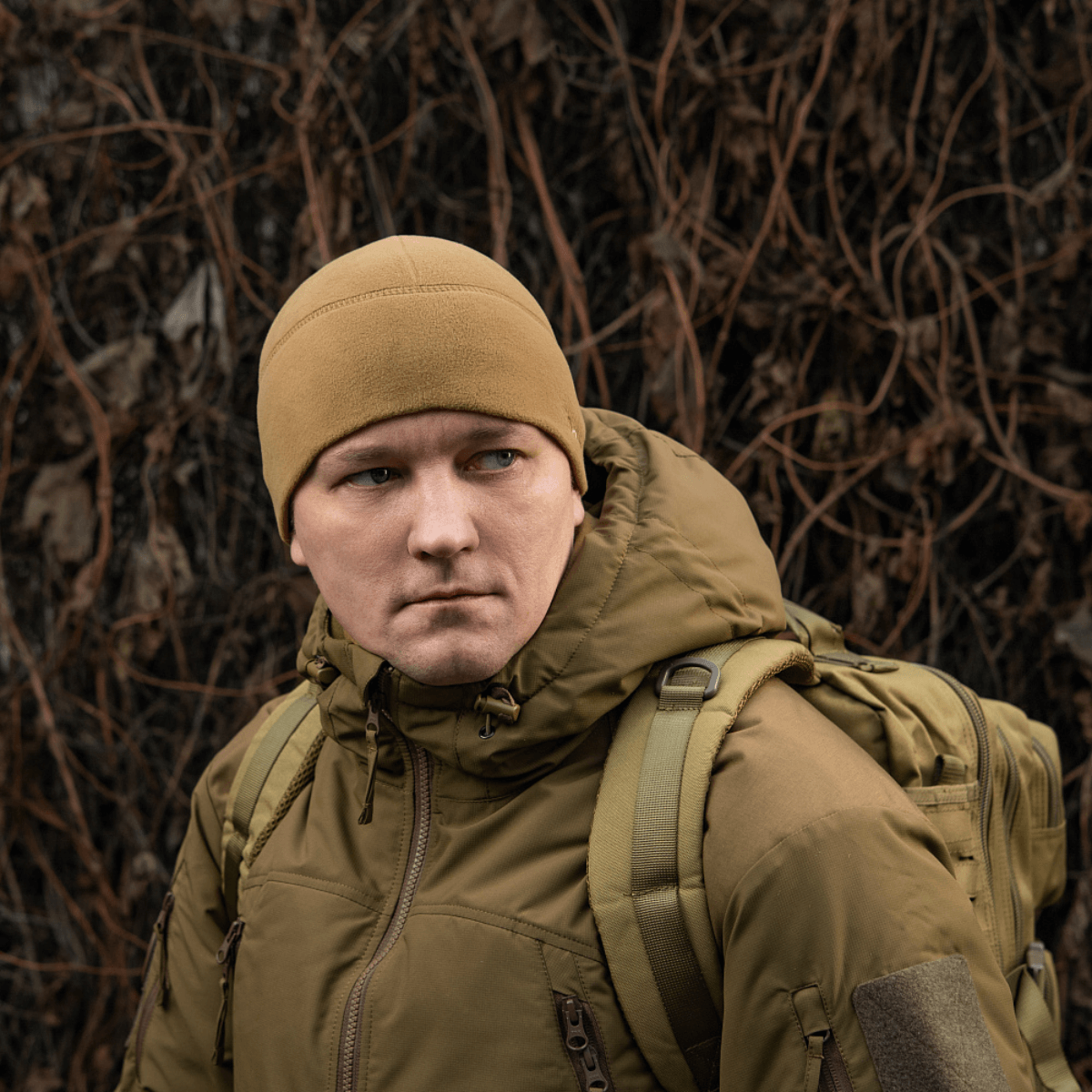 Mies pukeutuneena M-Tac Fleece Watch Cap Light Polartec talvihattuun luonnossa, repun kanssa. Sopii talvikäyttöön, valmistettu Polartec Micro Series fleece -materiaalista.