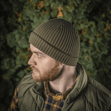 Mies käyttää M-Tac Watch Cap 100% Akryl -neulepipoa metsänvihreänä, tehty teollisesta kaksinkertaisesta akryylineuloksesta lämmöksi ja kestävyydelle.