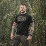 Mies M-Tac T-Shirt Logo -paidassa, camo-kuvio ja sloganit luonnossa.