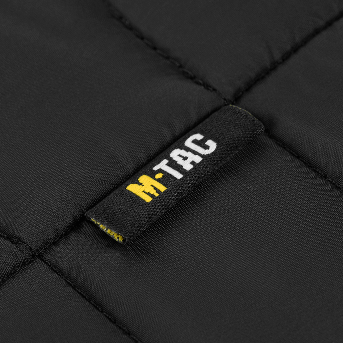 Yksityiskohta M-Tac-logosta mustalla kankaalla.