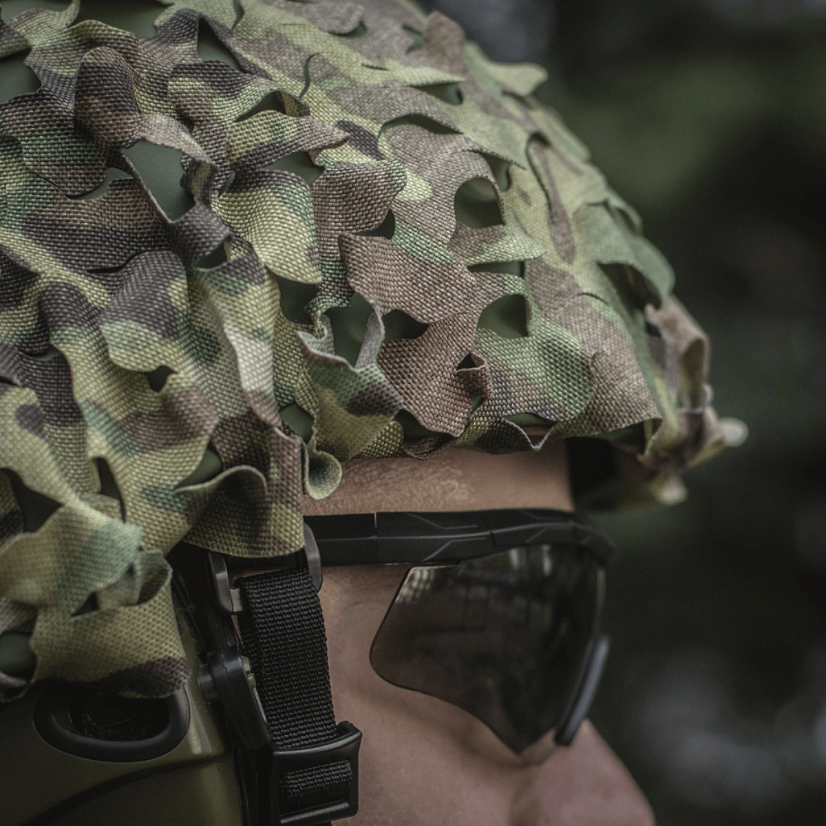 M‑Tac Vilha Hjelmcover Elite Multicam-camossa henkilöllä, valmiina suojaamaan kypärää likaa ja kulumista vastaan haastavissa olosuhteissa.