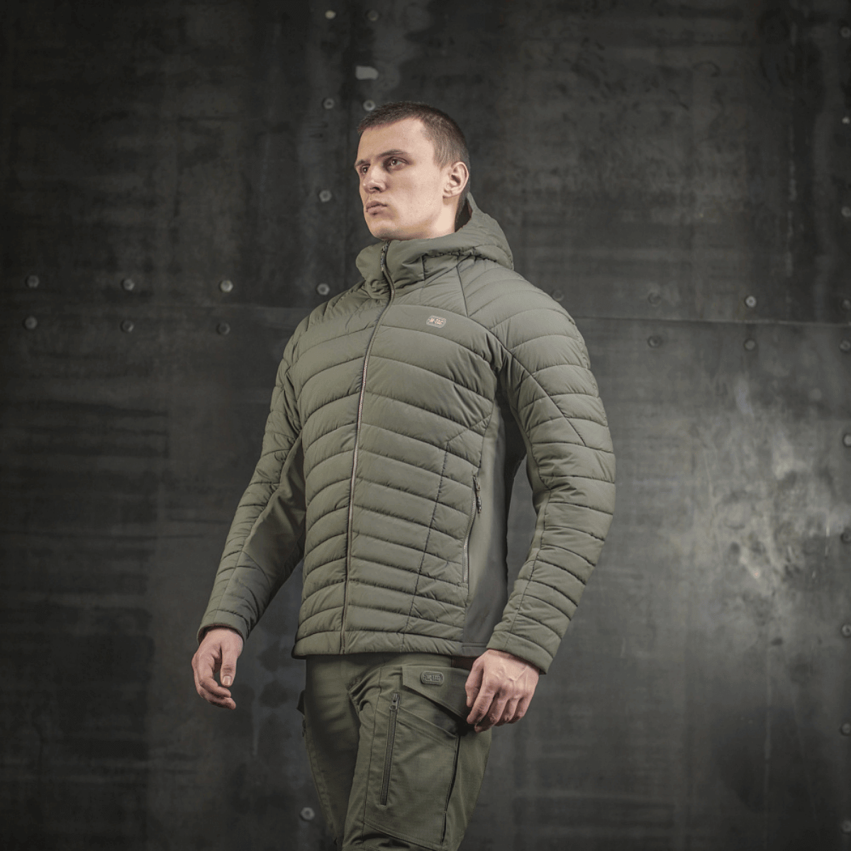 Mies pukeutuneena khakinväriseen M-Tac Jarl -takkiin, valmistettu Toray mechanical stretch -nylonista ja G-Loft-täytteellä maksimaaliseen lämpöön ja mukavuuteen.