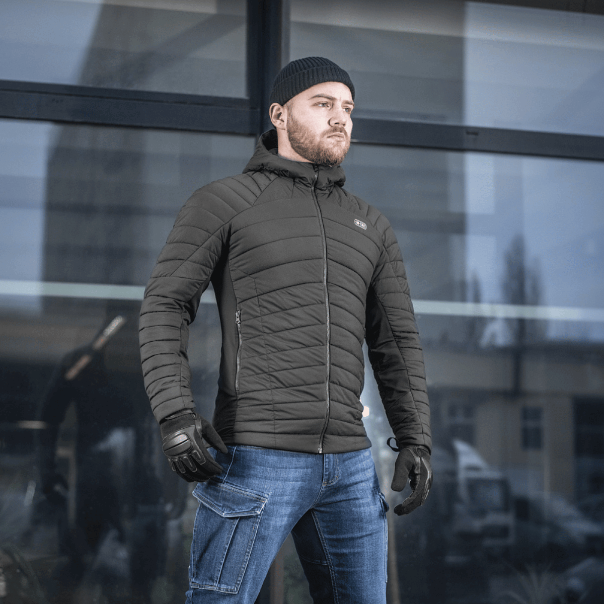 Mies pukeutuneena M-Tac Jarl -takkiin, monipuolinen välikausitakki G-Loft-eristyksellä suojaksi kylmää ja tuulta vastaan.